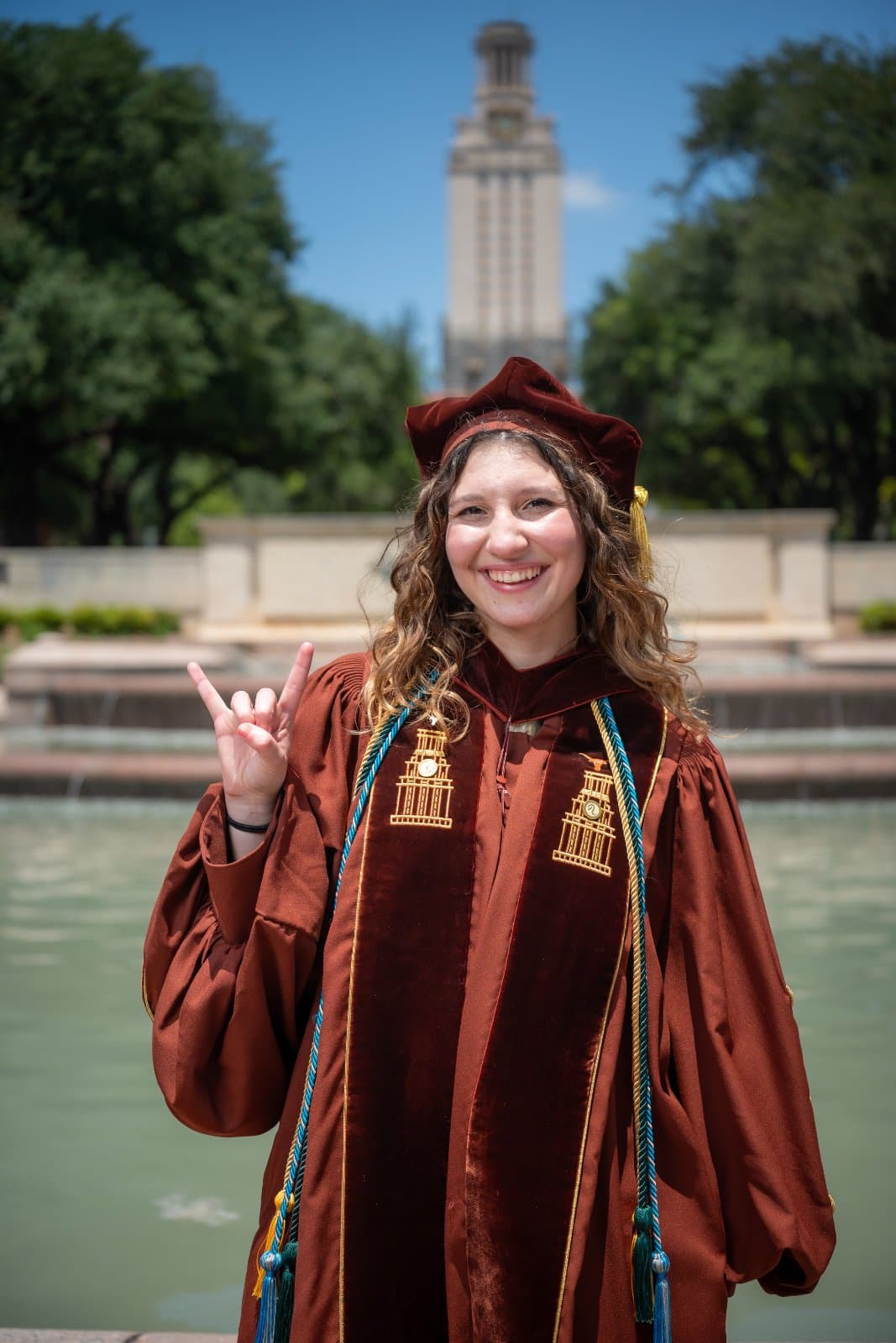 UT Austin graduation portrait with the Tower in the background and the graduate making the Hook ’Em Horns gesture — photographed by Zan Visuals.